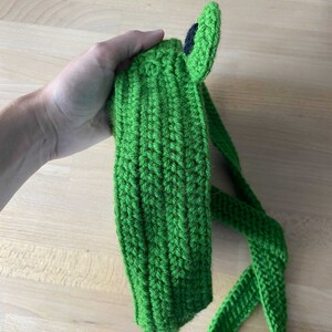 May include: Green crocheted frog headband with a black eye. The headband has a long green strap.