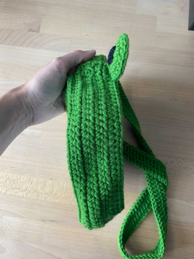 May include: Green crocheted frog headband with a black eye. The headband has a long green strap.