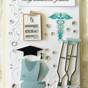 Può includere: Biglietto di auguri fatto a mano con la scritta "Congratulations Jessica!". Presenta decorazioni a tema medico: un blocco per prescrizioni, un caduceo, un cappello di laurea, una divisa chirurgica e delle stampelle, il tutto ornato da strass scintillanti.