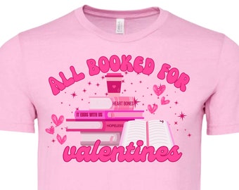 May include: Pink t-shirt with the text "All Booked for Valentines" in pink. The design features a stack of books with titles like "Heart Bones", "It Ends With Us", and "Hopeless", a coffee cup, and hearts.