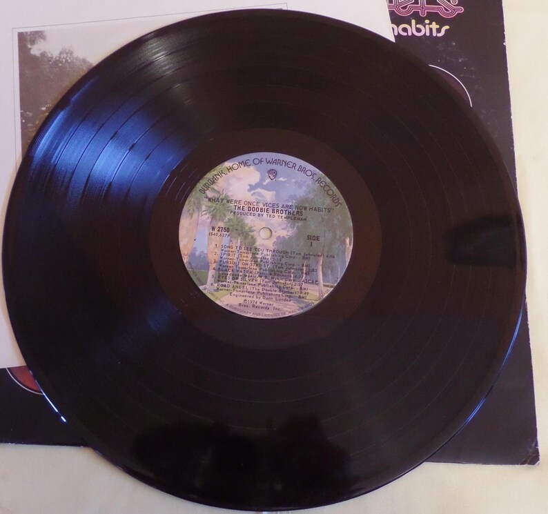 Puede incluir: Un disco de vinilo negro con una etiqueta blanca. La etiqueta tiene el texto "What Were Once Vices Are Now Habits" y "The Doobie Brothers".