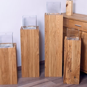 Könnte beinhalten: Vier Holzsockel mit durchsichtigen Glasbehältern darauf. Die Sockel sind aus hellbraunem Holz und haben eine natürliche Oberfläche. Die Behälter sind quadratisch und haben ein schlichtes Design.