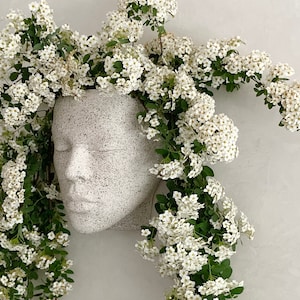 Pu&ograve; includere: Vaso da fiori in ceramica bianca a forma di viso con fiori bianchi a cascata dalla parte superiore.