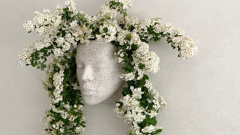 Pu&ograve; includere: Vaso da fiori in ceramica bianca a forma di viso con fiori bianchi a cascata dalla parte superiore.