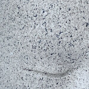Pu&ograve; includere: Primo piano di una superficie macchiata di bianco e grigio con un sottile motivo a onda. La superficie ha una texture ruvida.
