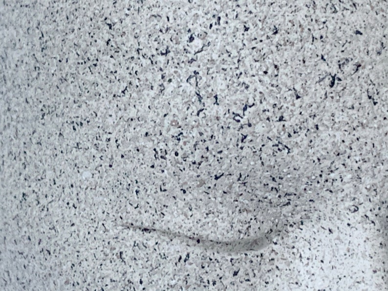 Pu&ograve; includere: Primo piano di una superficie macchiata di bianco e grigio con un sottile motivo a onda. La superficie ha una texture ruvida.
