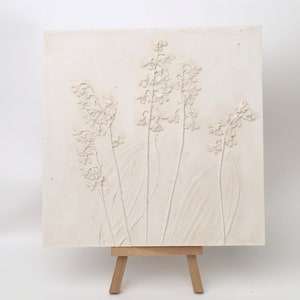 May include: White textured wall art featuring a raised relief design of lily of the valley flowers. The art is displayed on a small wooden easel.