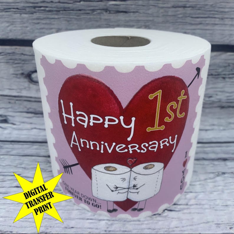 May include: A pink and white toilet paper roll with a red heart and gold lettering that says "Happy 1st Anniversary".  The heart has an arrow through it and two toilet paper rolls with faces are hugging.  The text below the heart says "One year down...forever to go!"