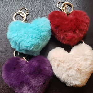 May include: Four heart-shaped fluffy keyrings in different colours: turquoise, red, beige, and purple. Each keyring has a gold metal ring.