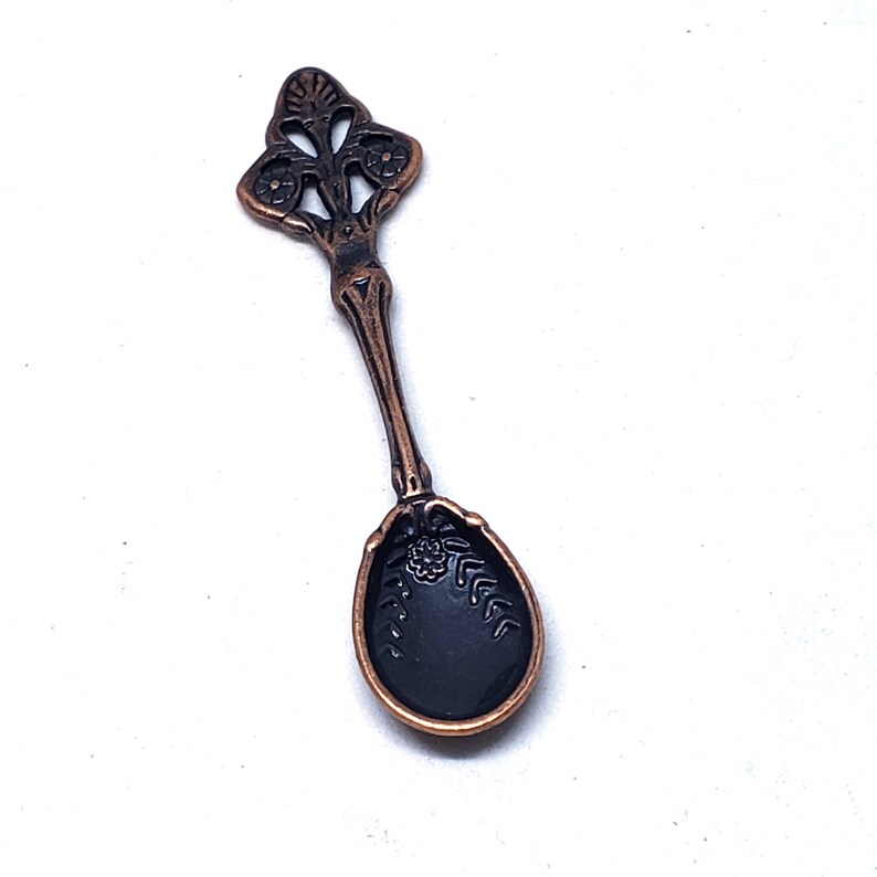 Peut inclure: Une petite cuill&egrave;re orn&eacute;e avec un manche noir d&eacute;taill&eacute; et un corps de couleur cuivre. La cuill&egrave;re a un motif floral d&eacute;coratif sur le manche.