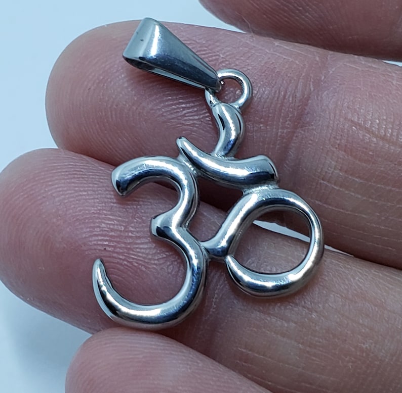 May include: A silver Om symbol pendant with a loop for a chain. The pendant is made of metal and has a shiny finish.