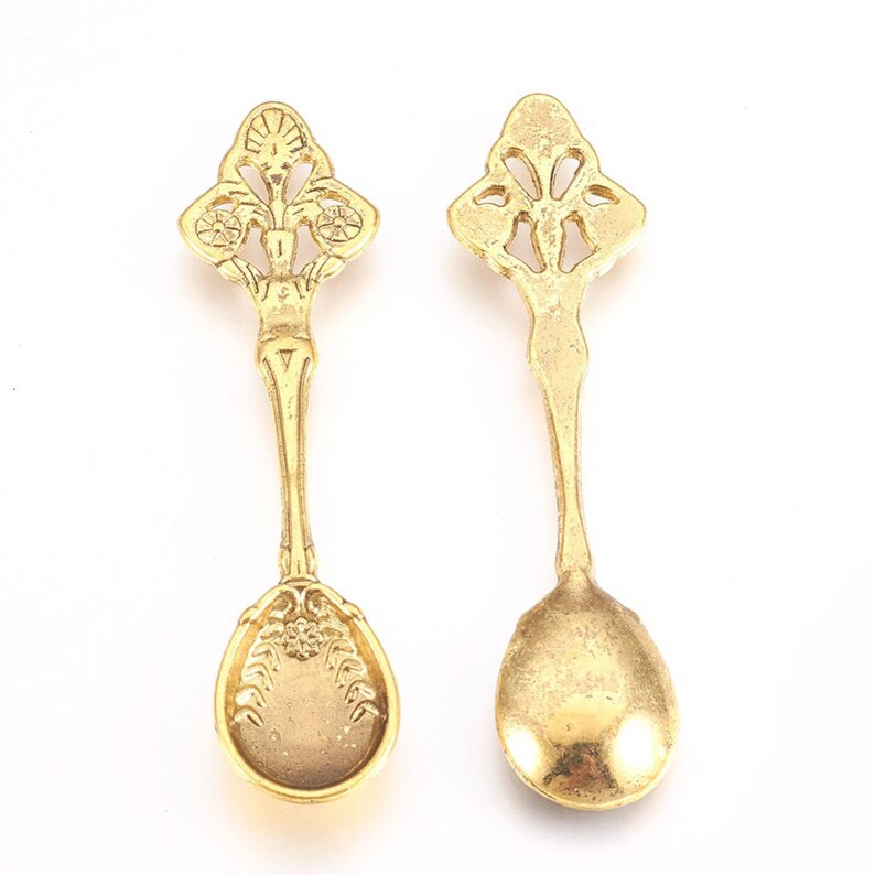 Peut inclure: Deux cuill&egrave;res d&eacute;coratives dor&eacute;es avec des manches orn&eacute;s et une t&ecirc;te de cuill&egrave;re arrondie. Les cuill&egrave;res sont sur un fond blanc.