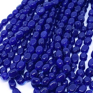 May include: Close-up of a collection of deep blue, oval-shaped beads. The beads are strung together, creating multiple strands. The glossy beads have a smooth texture and reflect light, suggesting a polished finish. These beads are suitable for jewelry making.