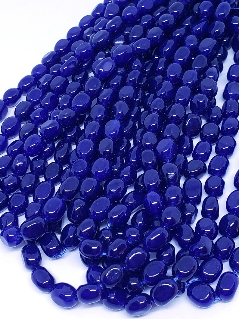 May include: Close-up of a collection of deep blue, oval-shaped beads. The beads are strung together, creating multiple strands. The glossy beads have a smooth texture and reflect light, suggesting a polished finish. These beads are suitable for jewelry making.