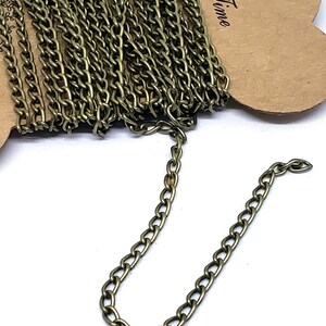 Puede incluir: Un rollo de cadena de oro antiguo, con una pequeña sección de la cadena extendida para mostrar el detalle. La cadena está empaquetada en una tarjeta marrón con la palabra "Time" escrita en ella.