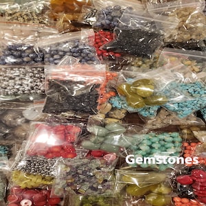 May include: Assortment of gemstones and beads in small plastic bags. The bags contain various colours and shapes of beads, including turquoise, green, red, and silver. The bags are labelled "Gemstones".