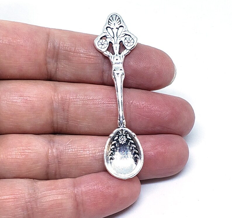 Peut inclure: Breloque cuill&egrave;re en argent avec un design orn&eacute;. La cuill&egrave;re a un bol arrondi et un manche d&eacute;coratif avec des d&eacute;tails floraux.