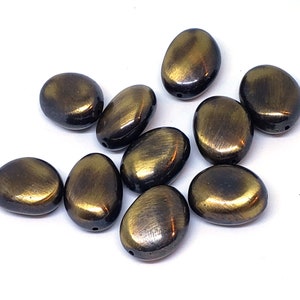 May include: Ten oval-shaped beads with a metallic gold finish. The beads have a slightly textured surface and a dark brown color.