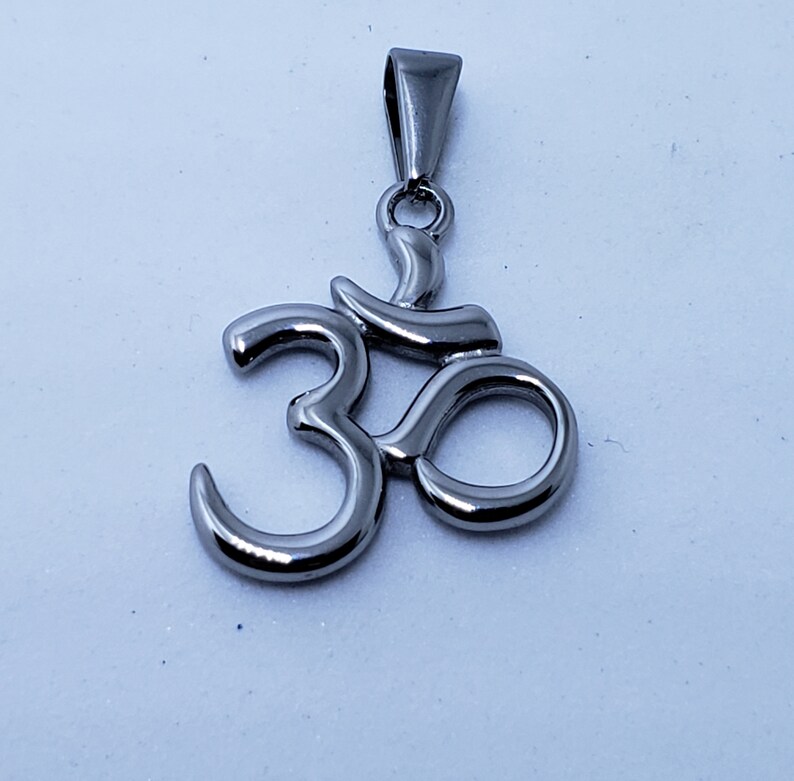 May include: A silver Om symbol pendant necklace. The pendant is a stylized representation of the Sanskrit word Om, which is a sacred sound in Hinduism and Buddhism.
