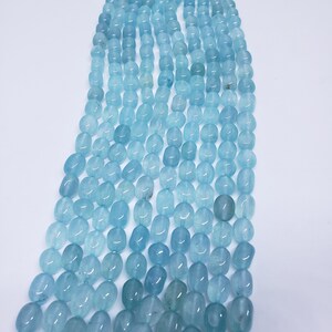 May include: Strands of aquamarine gemstone beads. The beads are oval-shaped and vary in shades of light blue. The beads are strung together, creating a cascading effect against a white background. Ideal for jewelry making.
