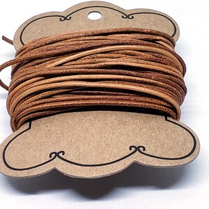 May include: A spool of brown leather cord wrapped around a cardboard tag with a hole in the center. The tag is shaped like a cloud with a decorative border.