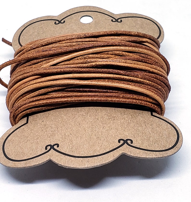 May include: A spool of brown leather cord wrapped around a cardboard tag with a hole in the center. The tag is shaped like a cloud with a decorative border.