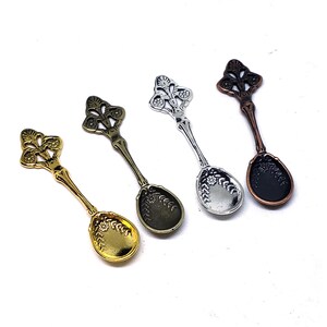 May include: Four ornate spoons with decorative handles. The spoons are in different finishes: gold, silver, bronze, and black.