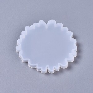 Puede incluir: Un molde de silicona blanco con forma de posavasos redondo y ondulado. El molde est&aacute; dise&ntilde;ado para crear un posavasos de resina con un borde &uacute;nico y org&aacute;nico.