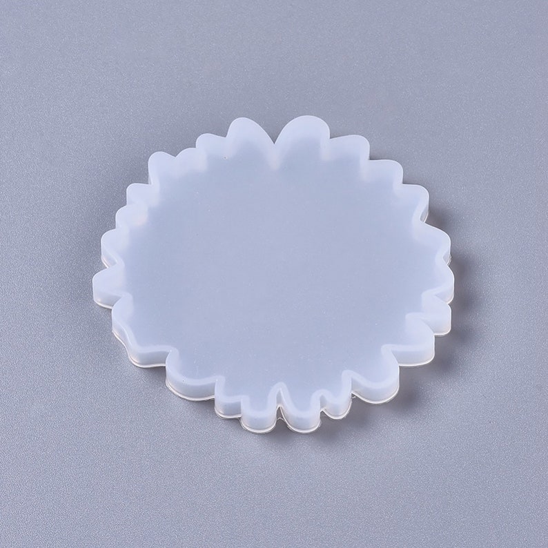 Puede incluir: Un molde de silicona blanco con forma de posavasos redondo y ondulado. El molde est&aacute; dise&ntilde;ado para crear un posavasos de resina con un borde &uacute;nico y org&aacute;nico.