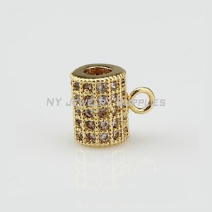 May include: Gold-toned metal bead with clear crystal accents. The bead has a cylindrical shape and a small loop on the side.