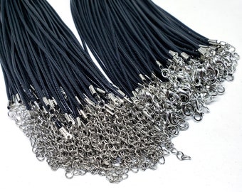 Puede incluir: Una colección de collares de cordón negro con cierres y extensores de cadena plateados. Los collares están cuidadosamente dispuestos, mostrando el contraste entre los cordones oscuros y los herrajes metálicos brillantes. Ideal para la fabricación de joyas.
