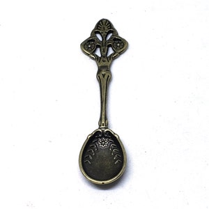Peut inclure: Une petite cuill&egrave;re orn&eacute;e de bronze avec un manche d&eacute;coratif et un bol arrondi. Le manche pr&eacute;sente un motif floral avec des d&eacute;tails complexes.