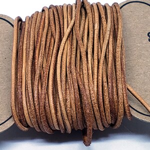 May include: A spool of brown leather cord. The cord is wound tightly and is ready to be used for crafting projects.