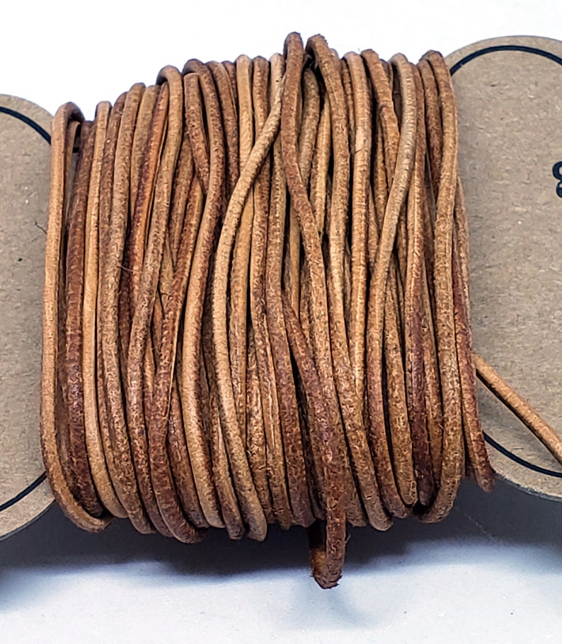 May include: A spool of brown leather cord. The cord is wound tightly and is ready to be used for crafting projects.