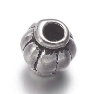 May include: A silver metal bead with a textured, rounded design. The bead has a hole in the center for stringing.