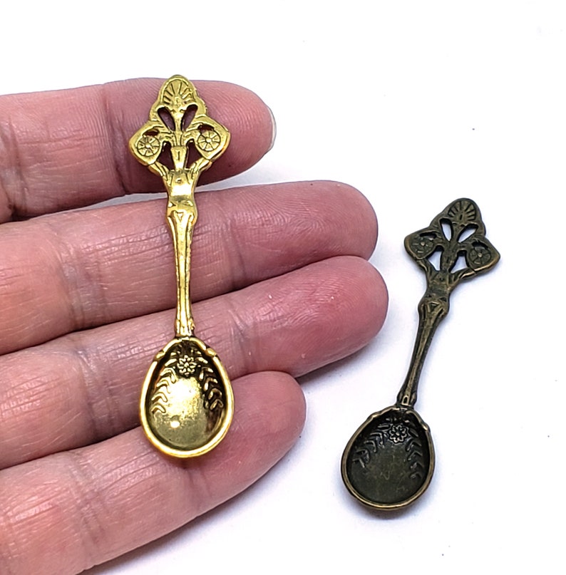 Peut inclure: Deux cuill&egrave;res en m&eacute;tal orn&eacute;es d'un motif floral d&eacute;coratif. La cuill&egrave;re de gauche est dor&eacute;e et celle de droite est en bronze.