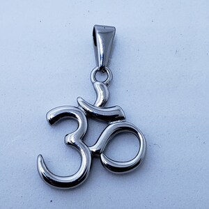 May include: A silver Om symbol pendant with a loop at the top for attaching to a chain.