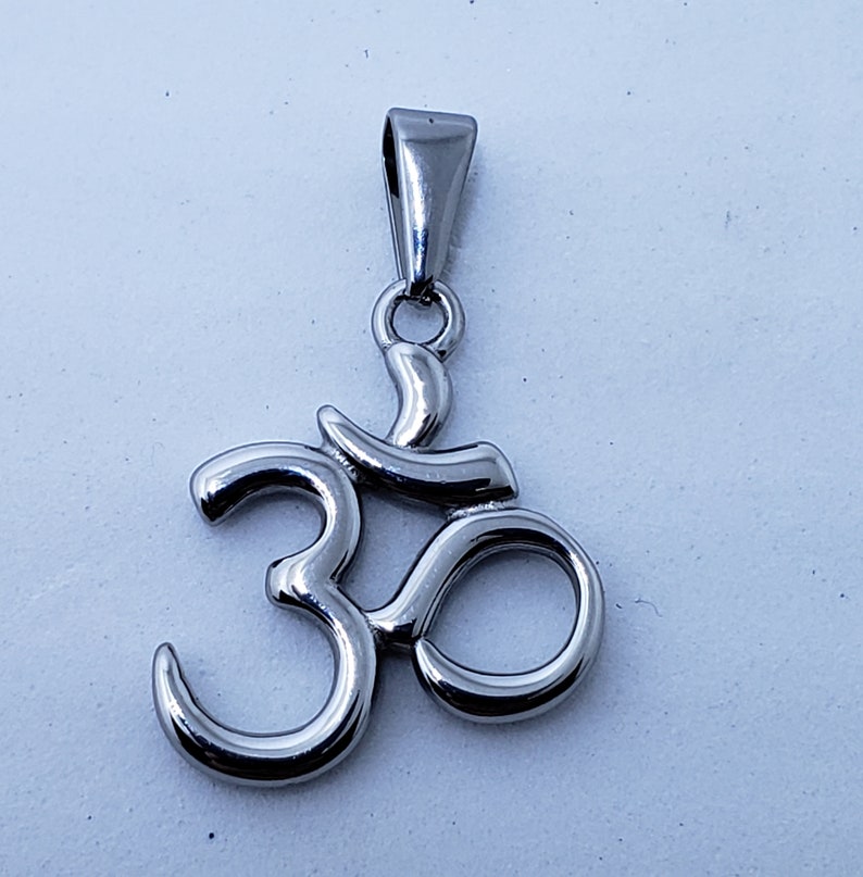 May include: A silver Om symbol pendant with a loop at the top for attaching to a chain.
