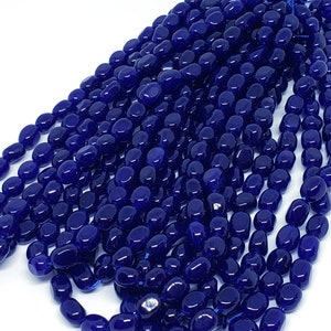 May include: A collection of deep blue, oval-shaped beads strung together. The beads have a glossy finish and are tightly packed, creating a dense, textured appearance. The beads are on a white background.