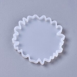 Puede incluir: Un molde de silicona blanco con un borde ondulado circular. El molde est&aacute; dise&ntilde;ado para crear posavasos de resina u otras artesan&iacute;as.
