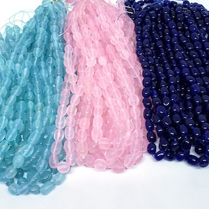 May include: Three strands of oval-shaped beads in light blue, pink, and navy blue. The beads are strung together, creating a cascading effect. The beads are smooth and have a glossy finish, ideal for jewelry making.