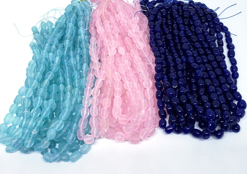 May include: Three strands of oval-shaped beads in light blue, pink, and navy blue. The beads are strung together, creating a cascading effect. The beads are smooth and have a glossy finish, ideal for jewelry making.