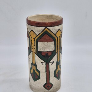 Peut inclure: Un vase cylindrique en céramique avec une base de couleur crème ornée d'un motif géométrique peint à la main en jaune, vert foncé et brun rougeâtre. Le bord est fini avec une bande brun rougeâtre unie et l'intérieur est beige clair.