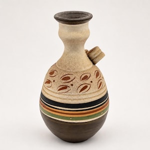 Peut inclure: Un vase en céramique avec un col étroit et un corps arrondi. La partie supérieure est de couleur crème avec des motifs en forme de feuilles brunes. La partie inférieure présente des rayures horizontales noires, orange, vertes et brun foncé.