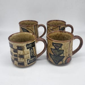 Puede incluir: Cuatro tazas de cerámica con asas marrones y exterior beige. Cada taza presenta diseños abstractos únicos en tonos marrones, negros y verdes. Las tazas son adecuadas para café, té u otras bebidas.