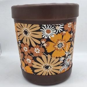 Peut inclure: Un pot en plastique brun avec un motif floral dans les tons orange, blanc et brun. Les fleurs sont stylisées et ressemblent à des marguerites.