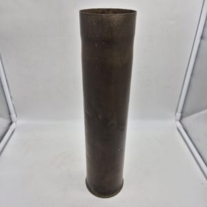 May include: A tall, cylindrical brass object with a slightly flared top and a rounded base. The brass has a dark, aged patina, suggesting it is vintage. The object is standing upright against a plain white background.