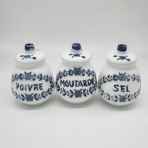 Puede incluir: Tres tarros de especias de cerámica blanca con diseños florales azules y etiquetas francesas: "POIVRE", "MOUTARDE" y "SEL".