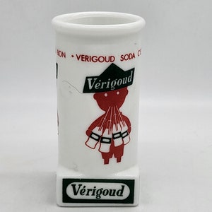 Può includere: Tazza in ceramica bianca con un'illustrazione rossa e nera di un personaggio dei cartoni animati che tiene bottiglie di soda. Il testo "Vérigood" è stampato in nero su sfondo verde nella parte inferiore della tazza.