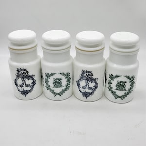 Puede incluir: Conjunto de cuatro tarros de especias de cerámica blanca con diseños florales verdes y negros. Cada tarro tiene una tapa blanca.